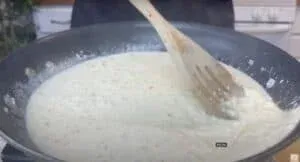 Stirring creamy risotto in a black pan with a wooden spoon on a stove.